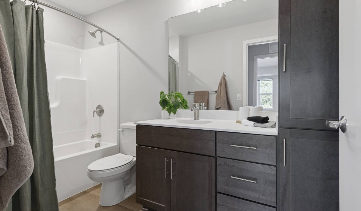 Modern bathroom with dark wood cabinets, white countertop, bathtub, green shower curtain, and potted plant.