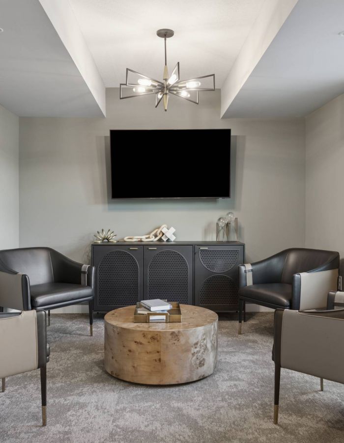 Modern lounge with four armchairs, round wooden coffee table, TV, and large window letting in natural light.