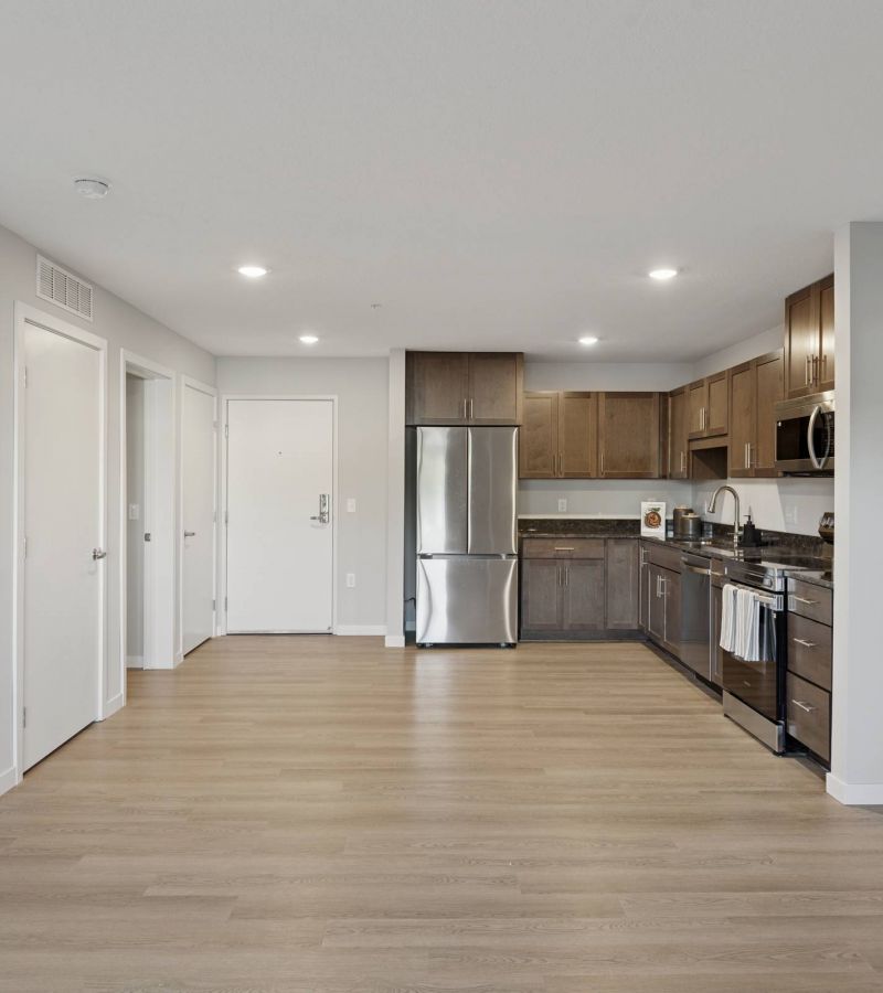 Modern kitchen with stainless steel appliances, wood cabinets, and light wood flooring in open apartment.