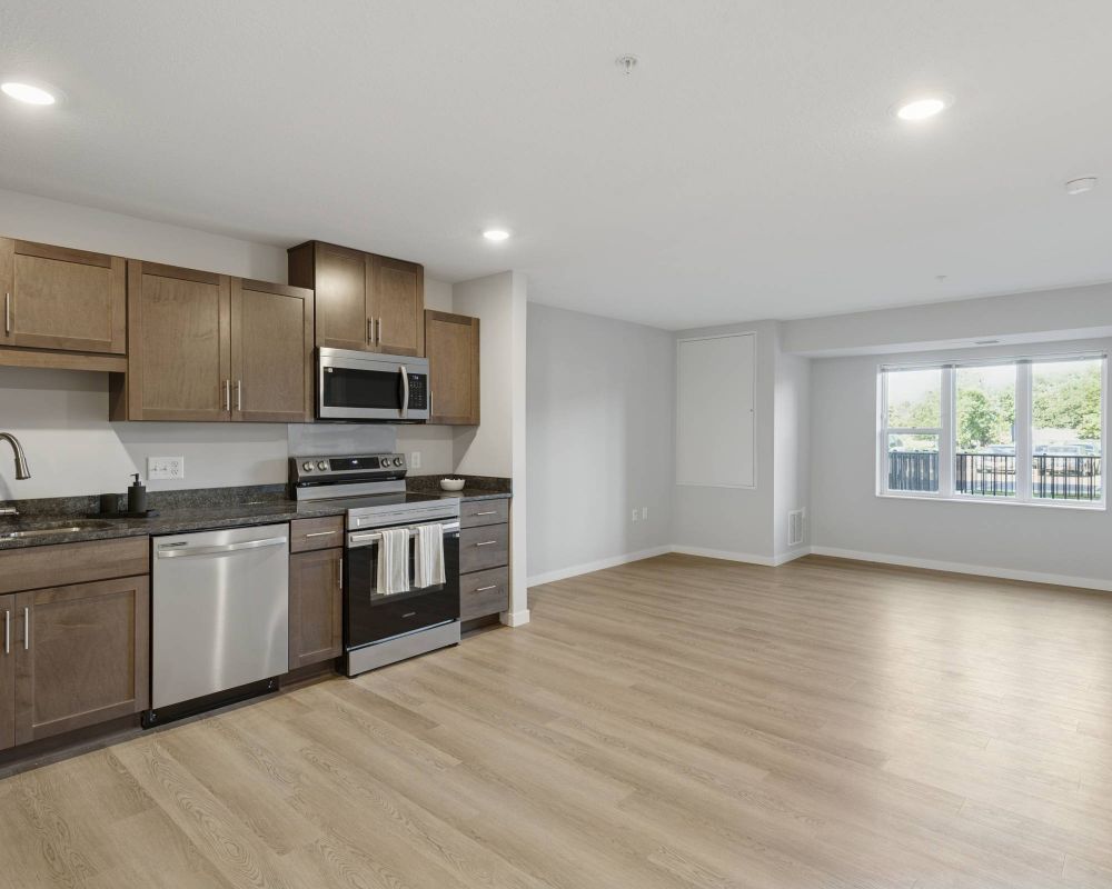 Modern kitchen with wood cabinets, stainless steel appliances, and an open living area with large windows.