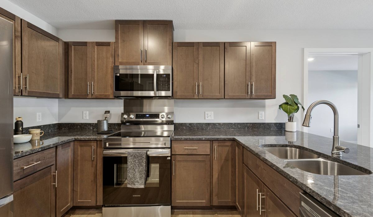 Modern kitchen with brown cabinets, stainless steel appliances, and a double sink with a potted plant nearby.