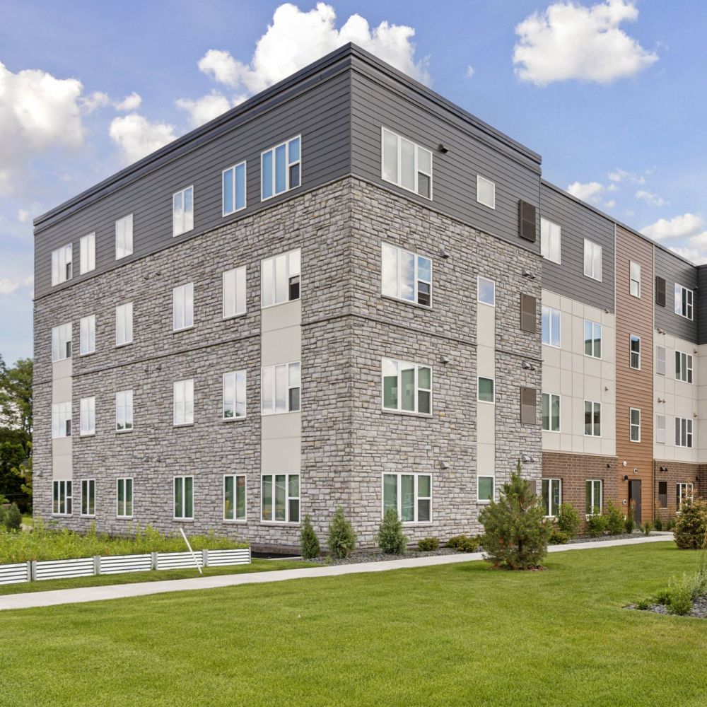Four-story modern apartment building with a sign reading "Callisto Commons 6257" on a green lawn.