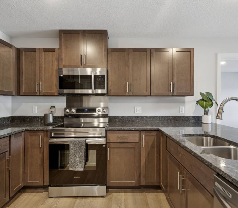 Modern kitchen with brown cabinets, stainless steel appliances, and a double sink with a potted plant nearby.