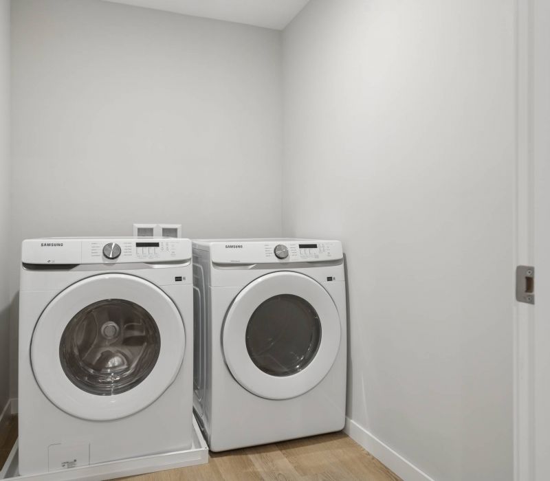 A laundry room with a front-loading washer and dryer side by side on a wood floor.