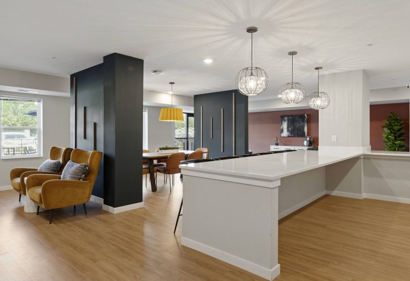 Modern open-concept living space with mustard chairs, dining area, and pendant lights over a white island.